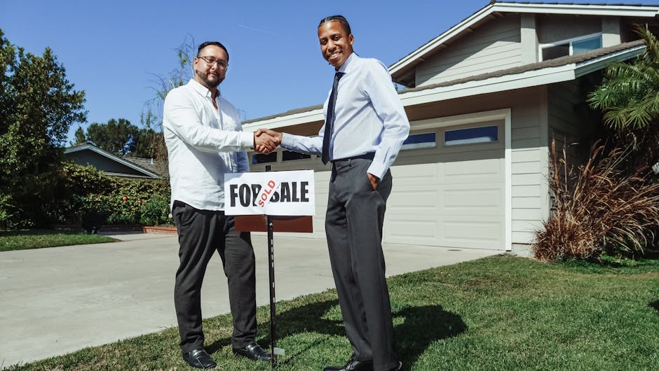 Two men shake hands in front of a new home with a sold sign, symbolizing a successful real estate deal